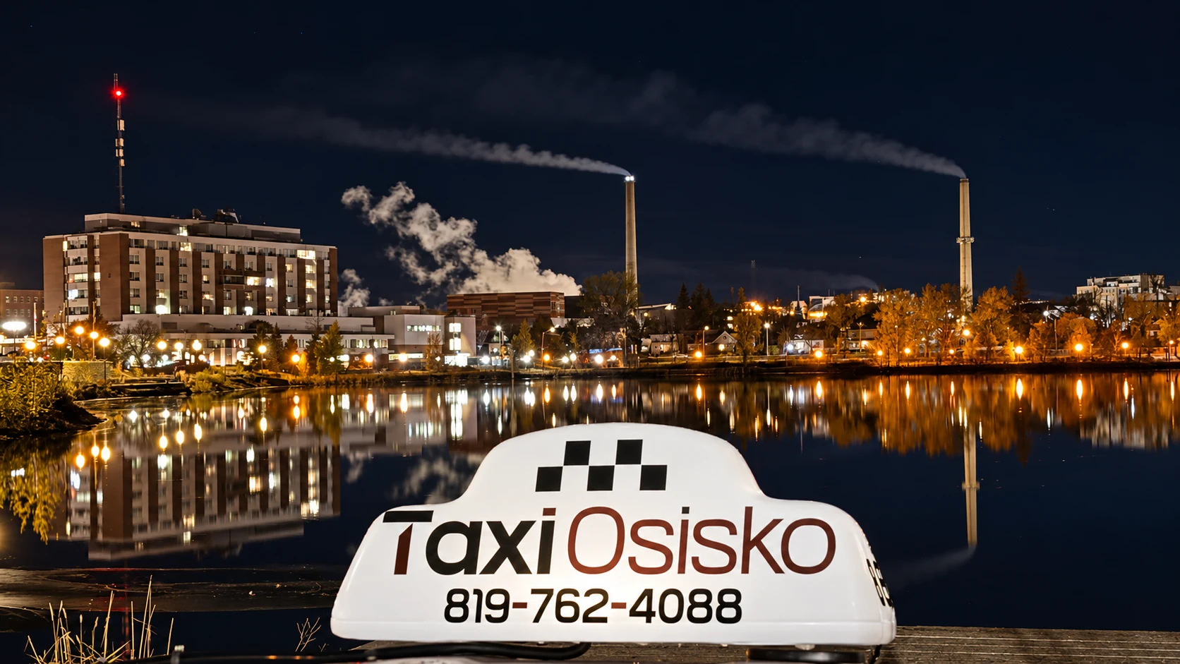 L’enseigne Taxi Osisko devant les lumières de Rouyn-Noranda et leurs reflets sur le lac